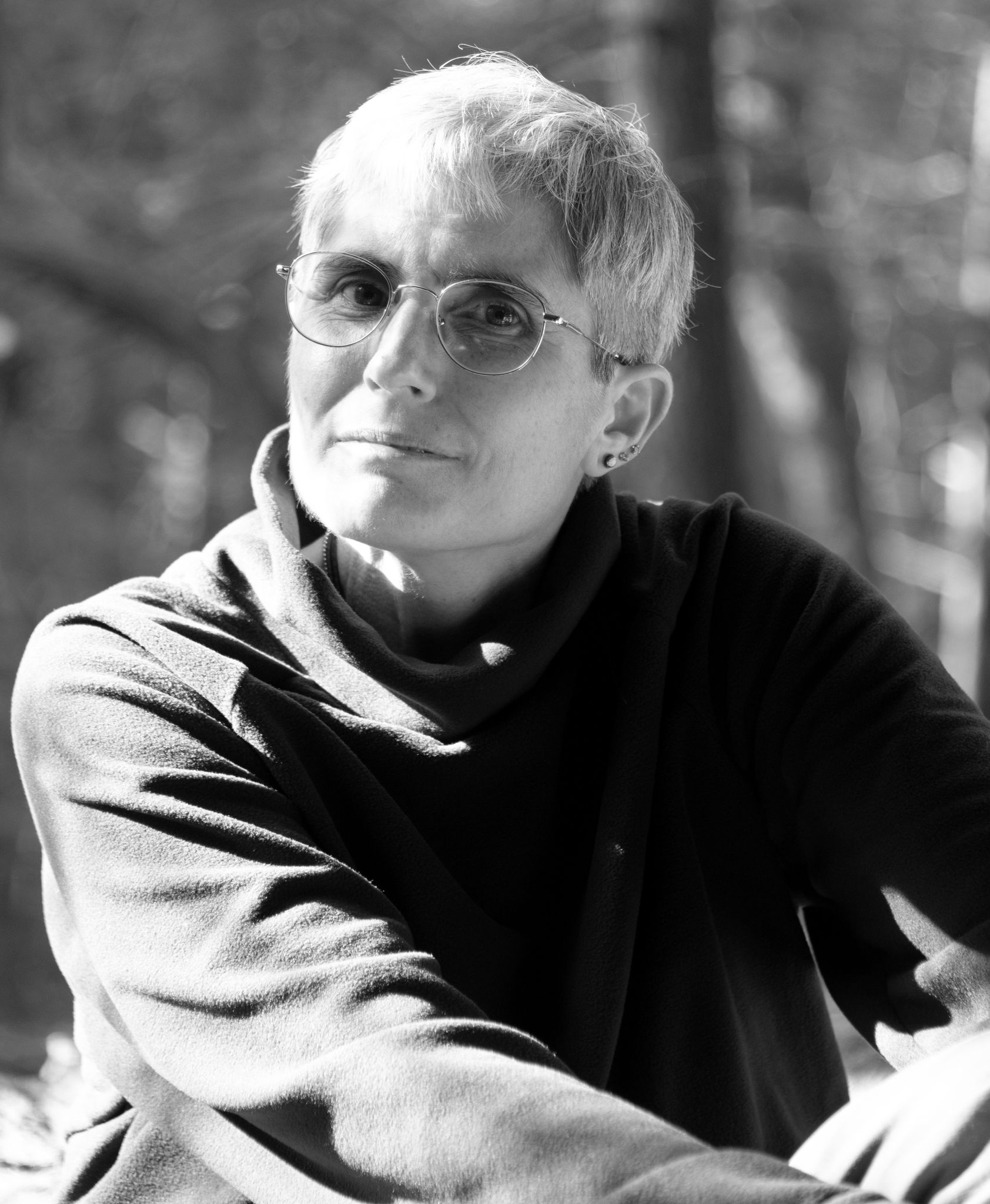A white woman with short hair wears round glasses and a black sweater. She gazes at the camera. The photo is in black and white.