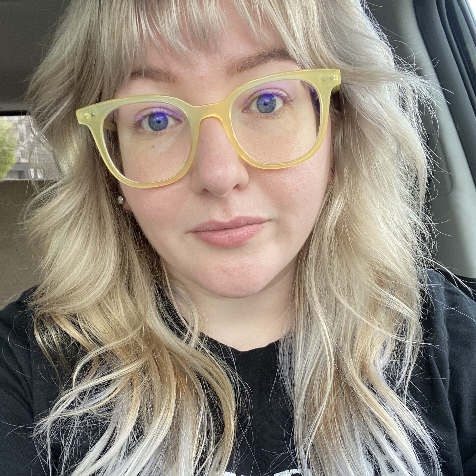 A white person with yellow-rimmed glasses and long, blonde hair. Their shirt reads, "THE FUTURE IS NONBINARY."