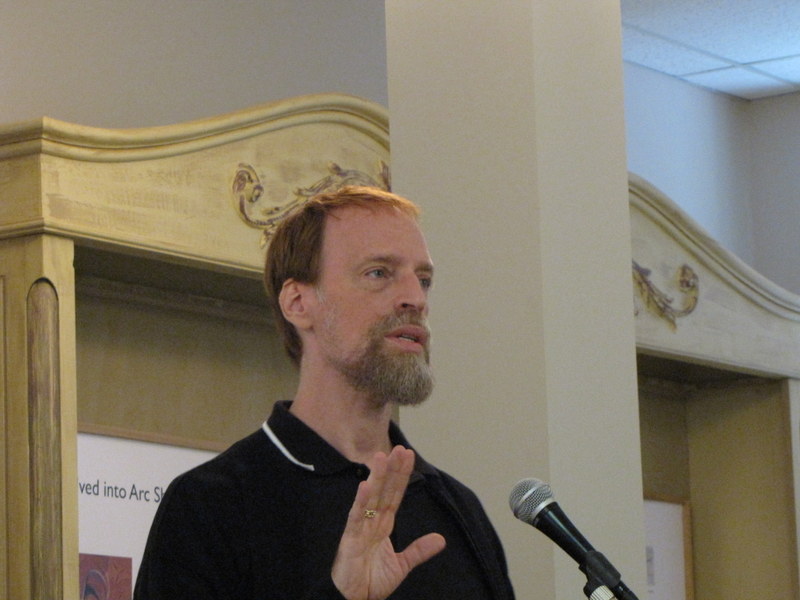 A white man with ginger hair and a beard speaking into a microphone.