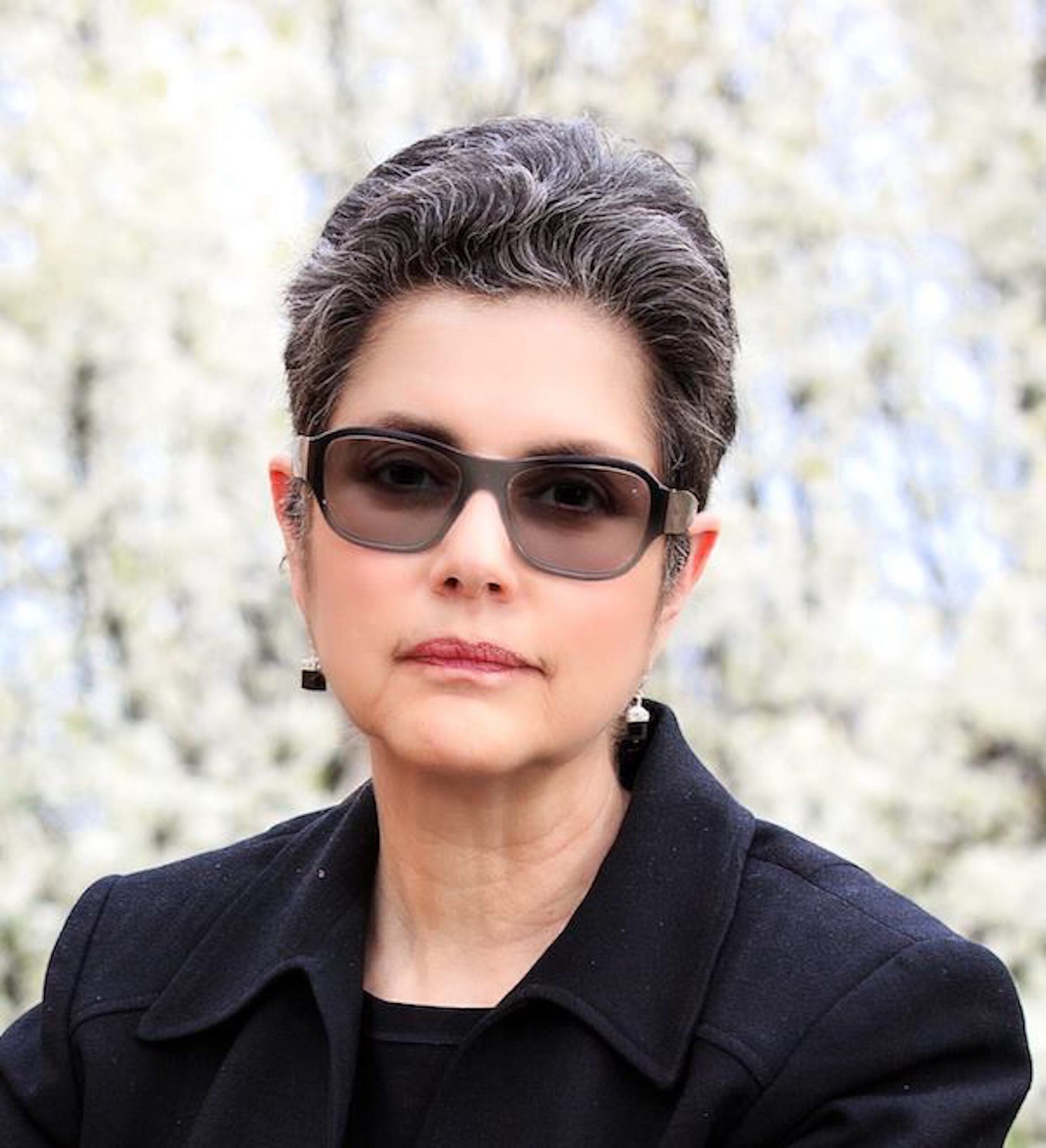 A white woman with short, gray hair wearing sunglasses and a black jacket.