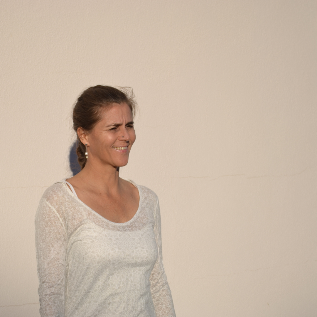 A white woman with dark hair is smiling and looking off-camera. She wears a white, long sleeved shirt.