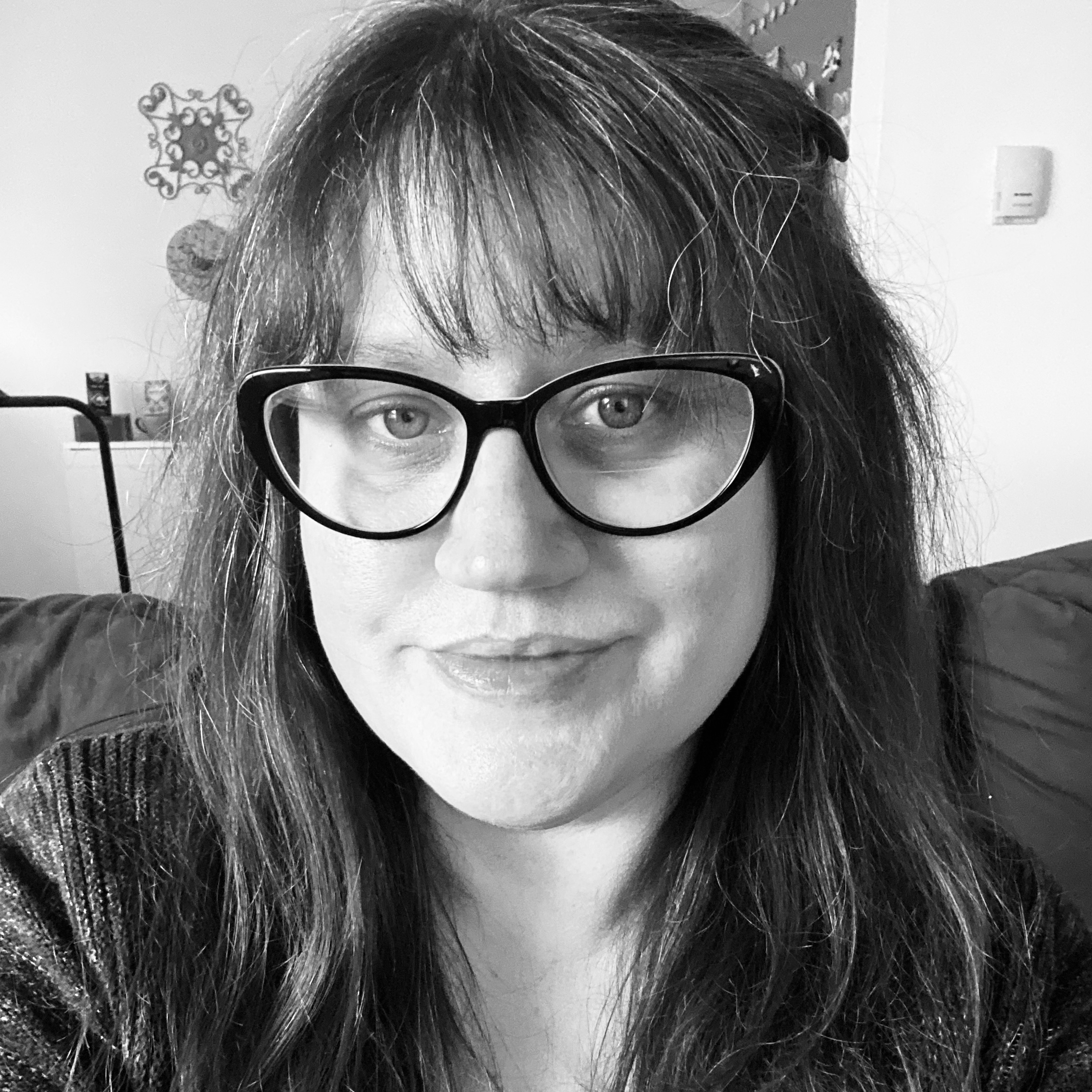 A black and white photo of a white woman with glasses smiling with her mouth closed.