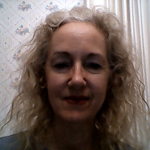 A white woman with gray hair smiling with her mouth closed at the camera.