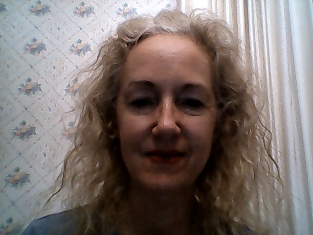 A white woman with gray hair smiling with her mouth closed at the camera.