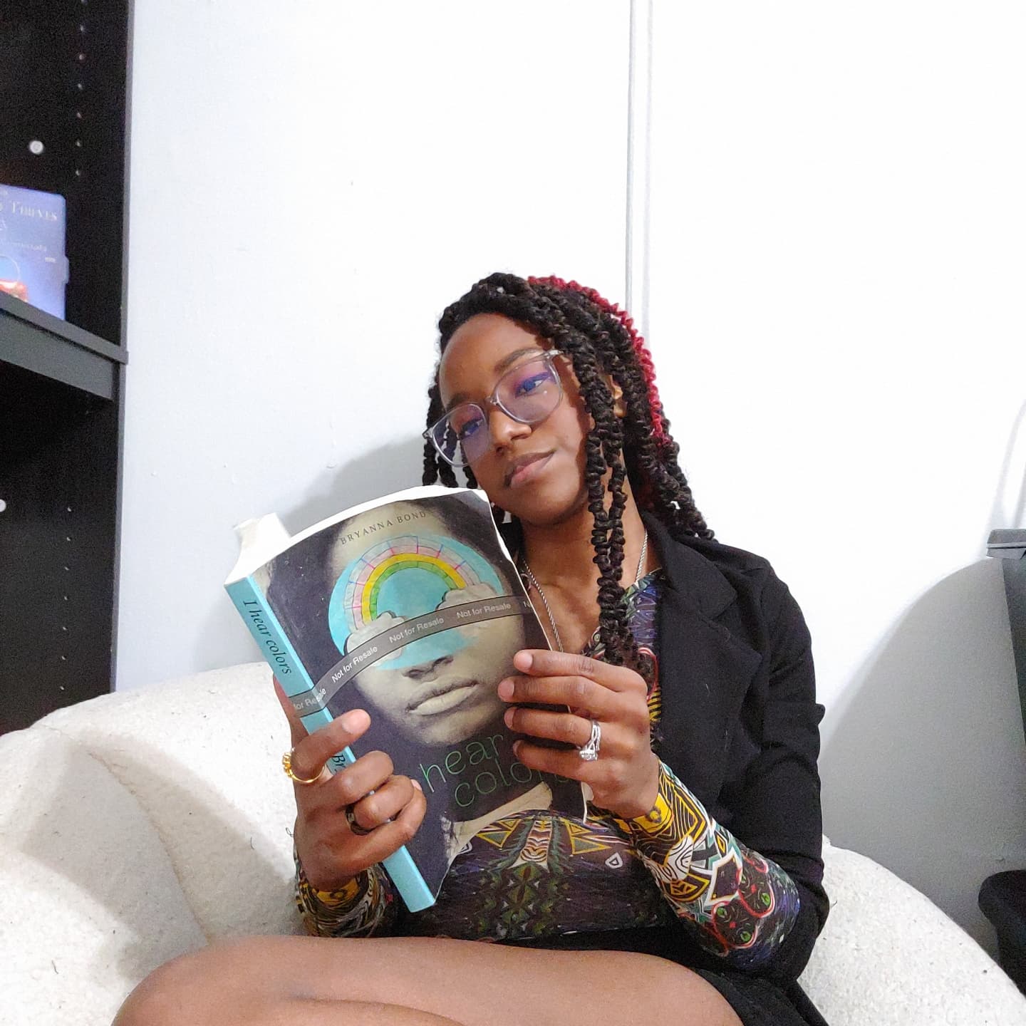 A Black woman with long, dark brown hair reading a book on a white chair.