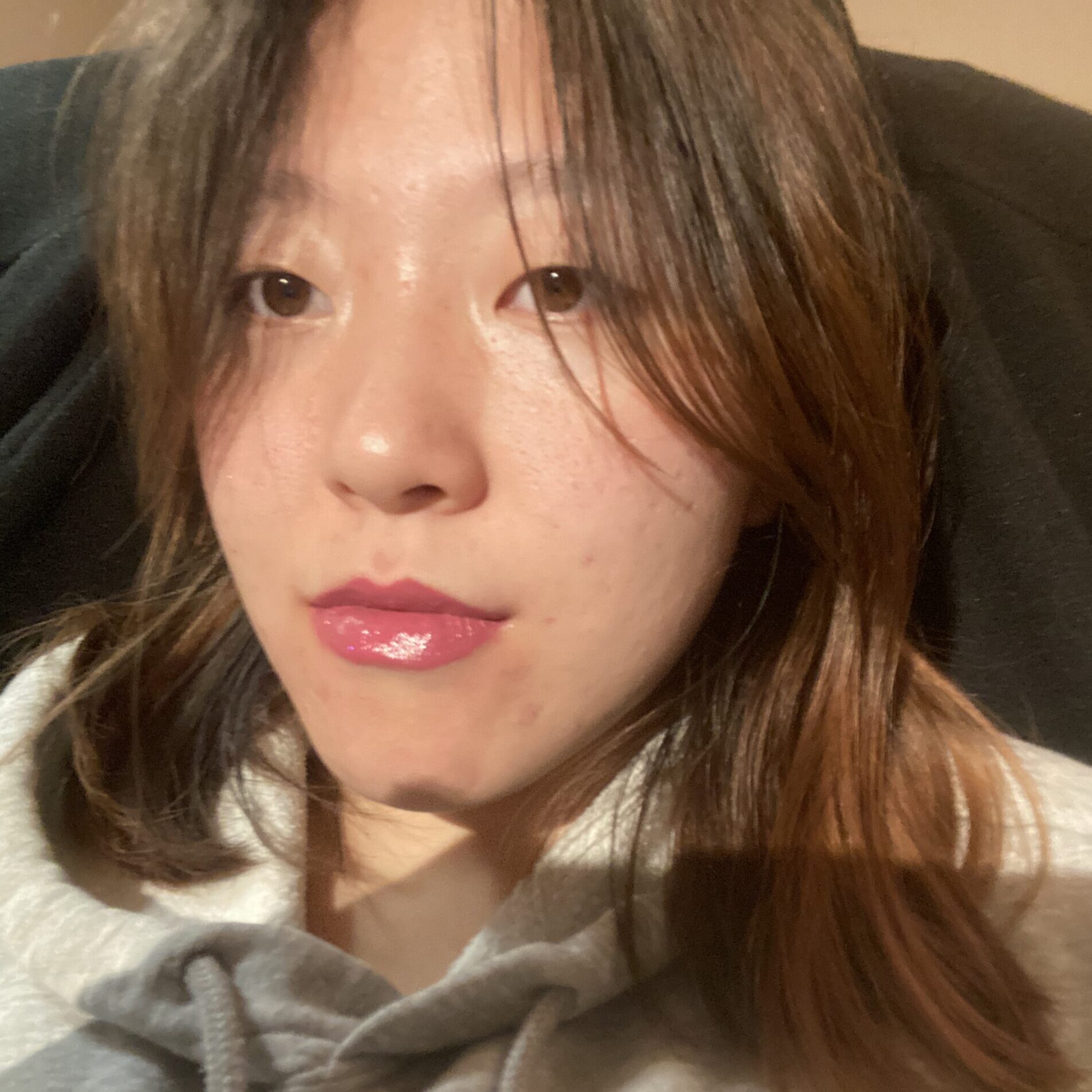 A photo of a young Asian woman with long, brown hair gazing at the camera. She is wearing a white shirt. The photo appears to have been taken as a selfie.